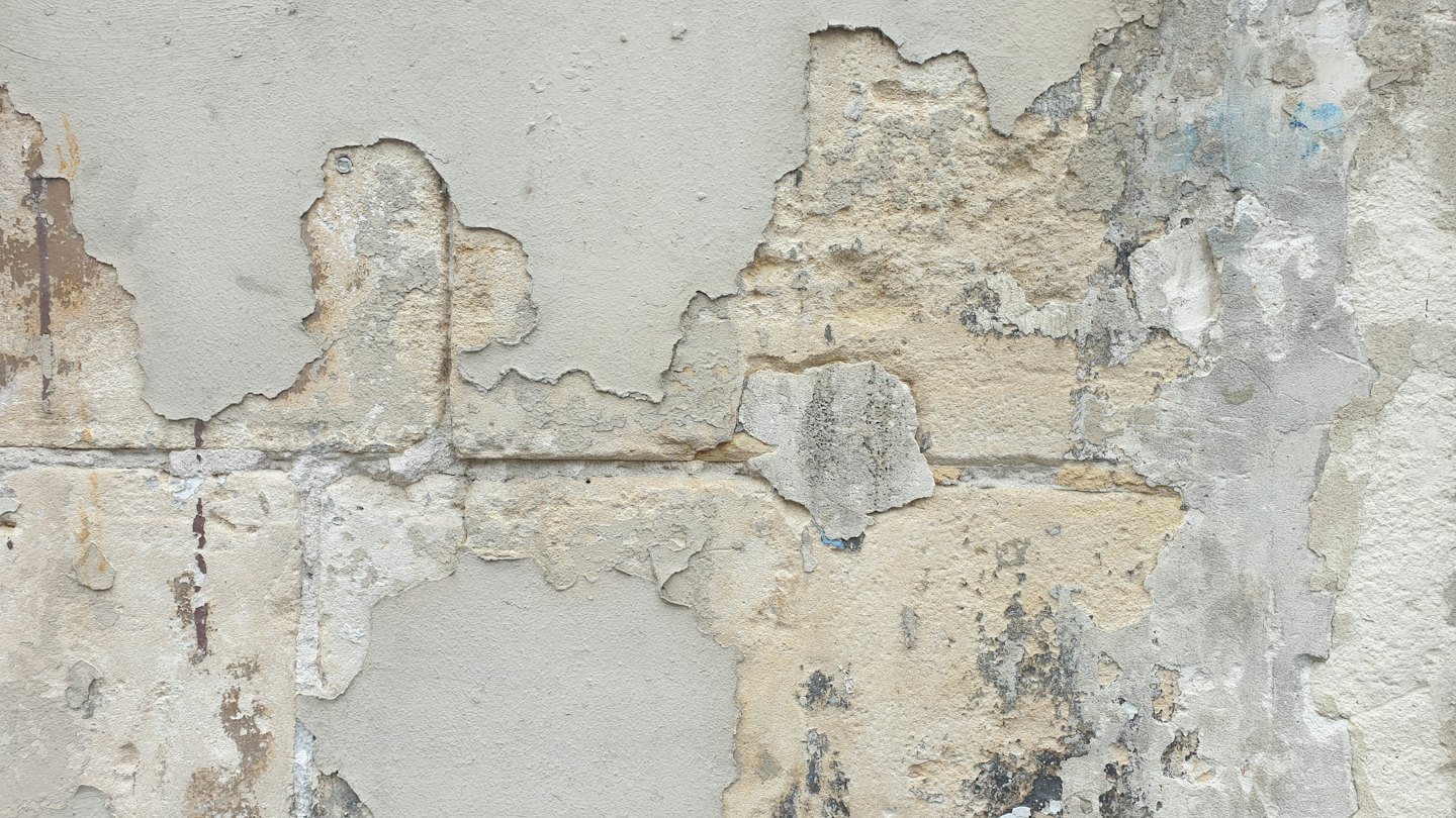 Peeling plaster reveals old brickwork on a weathered building exterior.