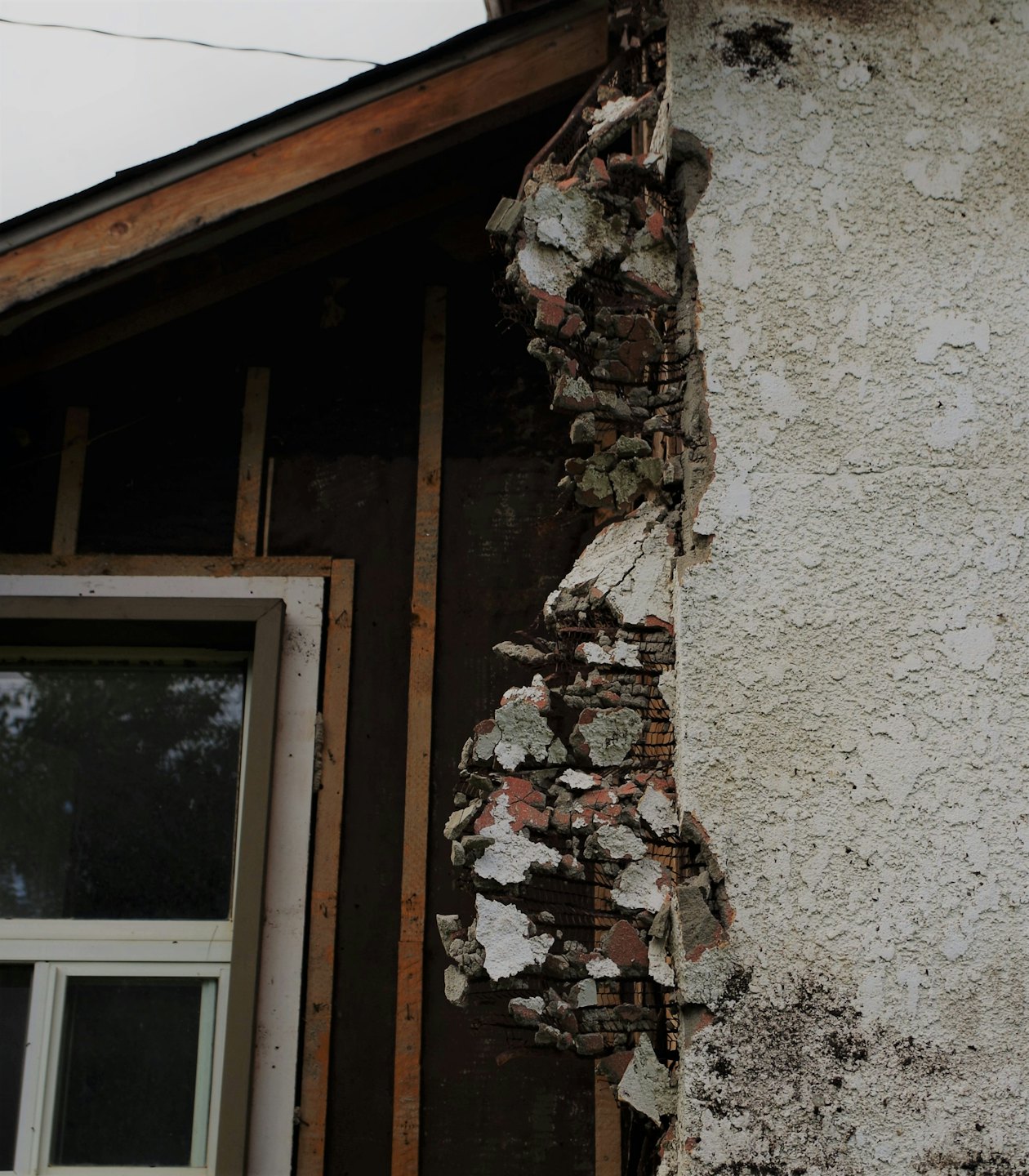 Damaged white stucco peels from a building to show red brick.