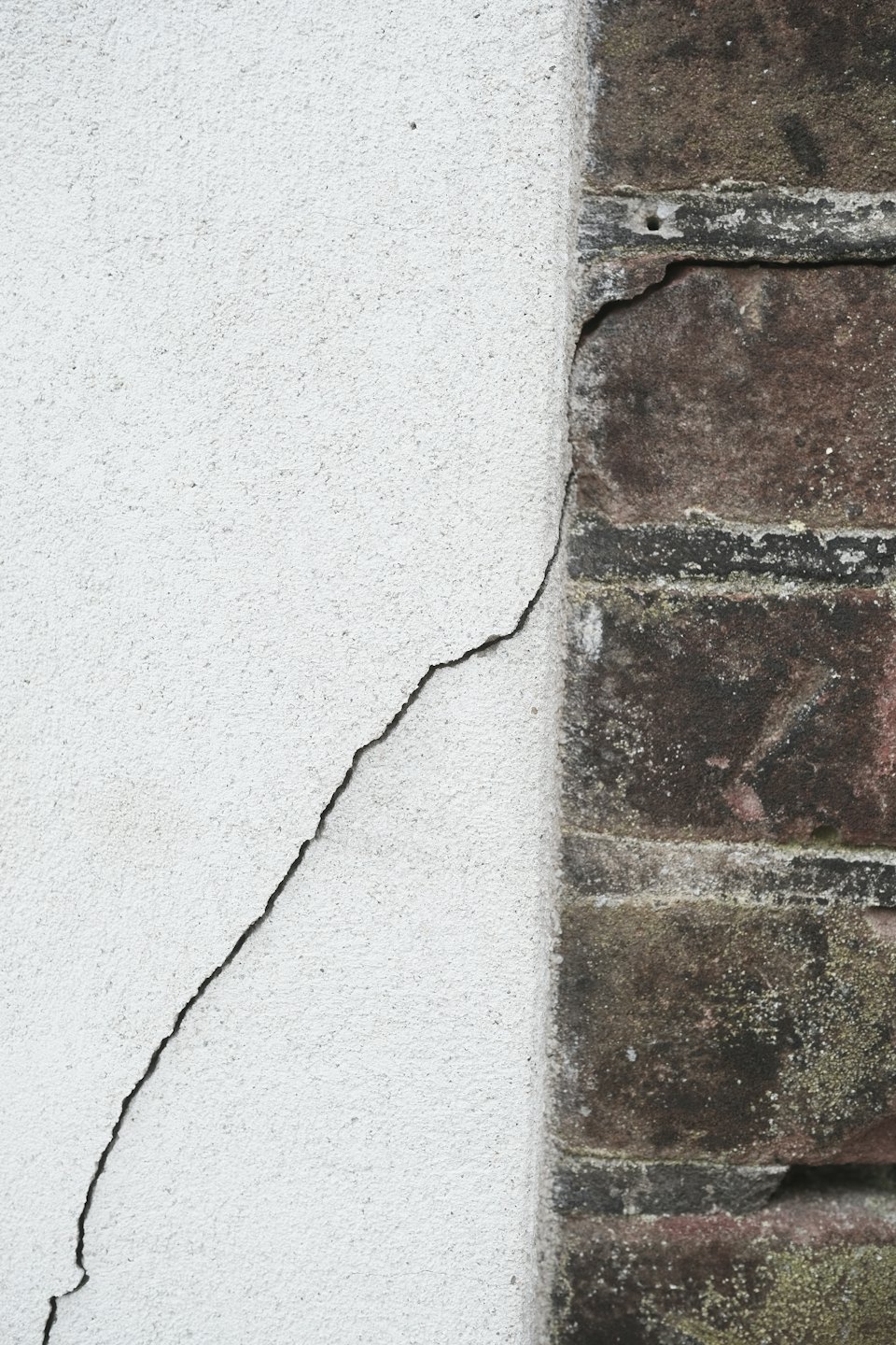 A diagonal crack runs through weathered brick and white stucco walls.